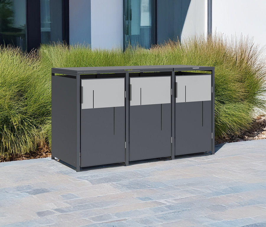 Drei graue Mülltonnen zur Mülltrennung stehen nebeneinander auf einer gepflasterten Fläche vor einem Gebäude und Gras.