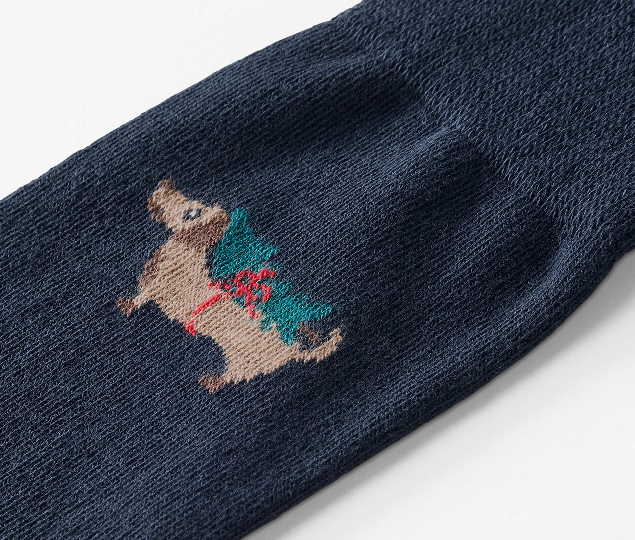 Detailaufnahme einer blauen Socke mit der Stickerei eines Igels, der einen Weihnachtsbaum trägt.