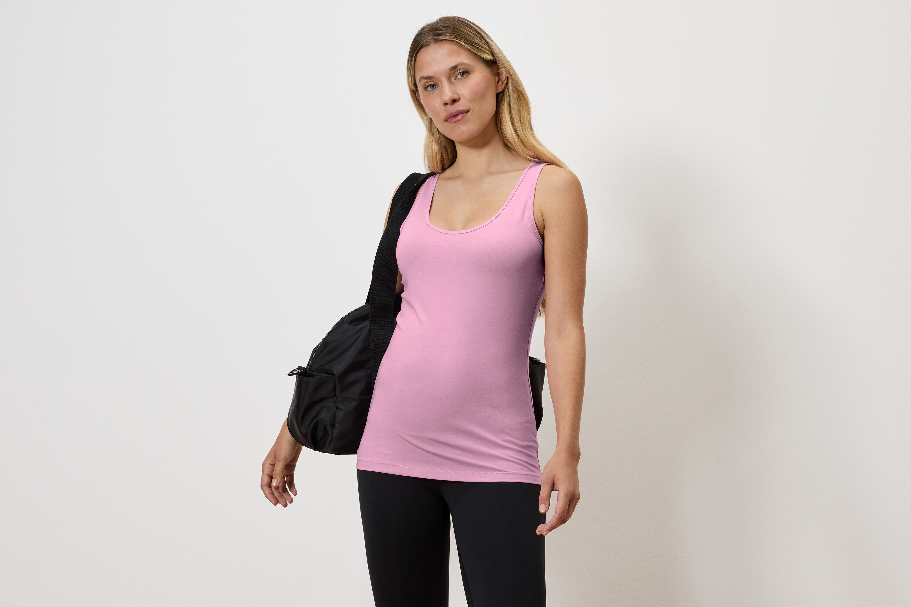 Frau in rosa Tanktop und schwarzen Leggings mit schwarzer Tasche über der Schulter.