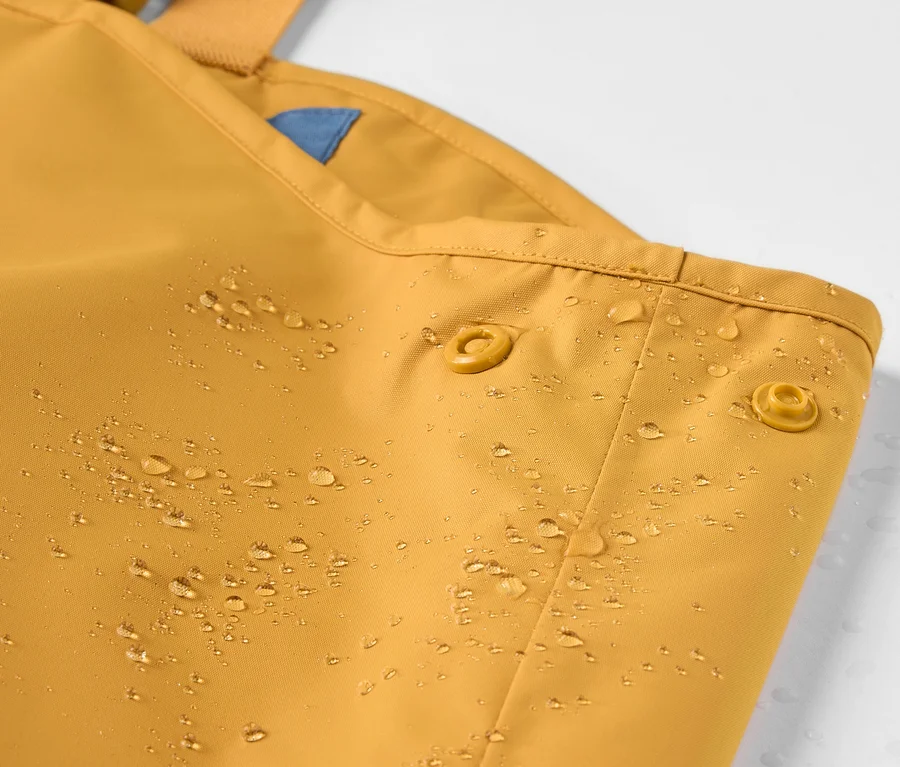 Detailaufnahme einer Kinder-Regenhose mit Wassertropfen.