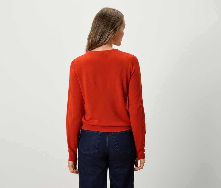 Rückansicht einer Frau mit einem orangefarbenen Pullover und dunkelblauen Jeans.