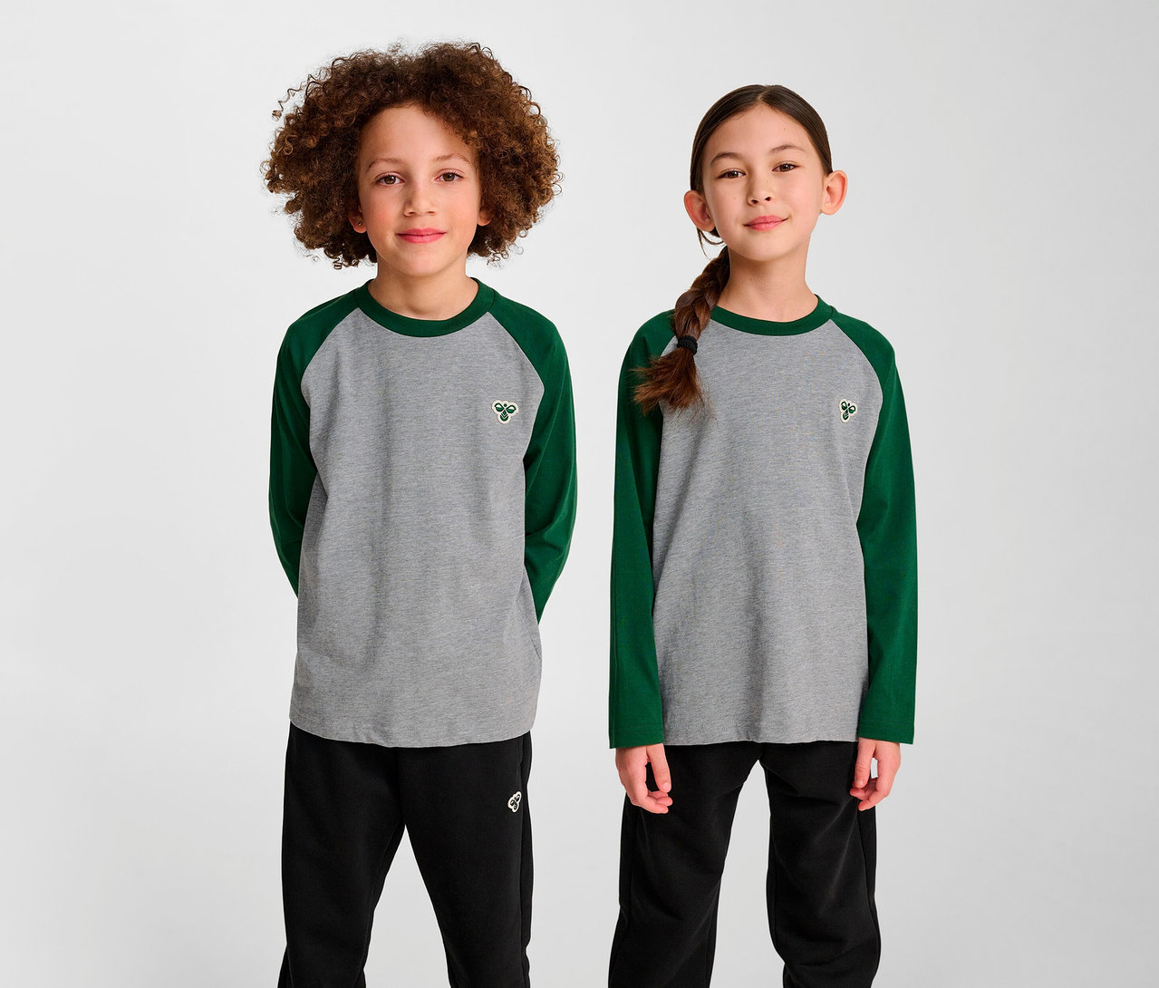 Zwei Kinder stehen nebeneinander und tragen grüne HUMMEL HMLJR Raglan Loose T-Shirts.