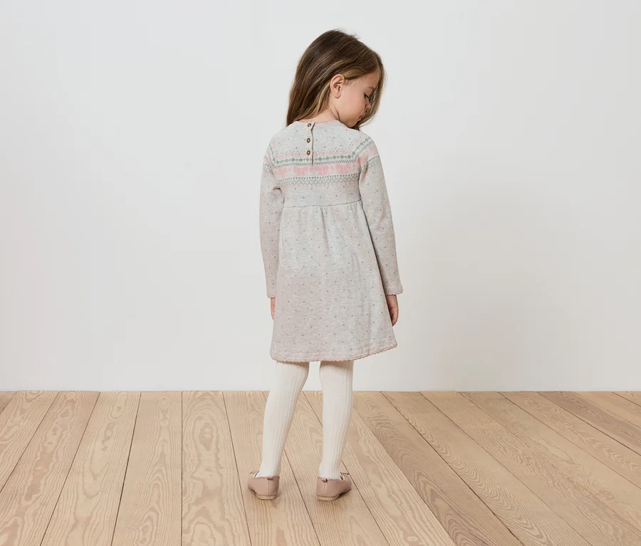Mädchen in langärmligem Kleid steht mit dem Rücken zur Kamera.
