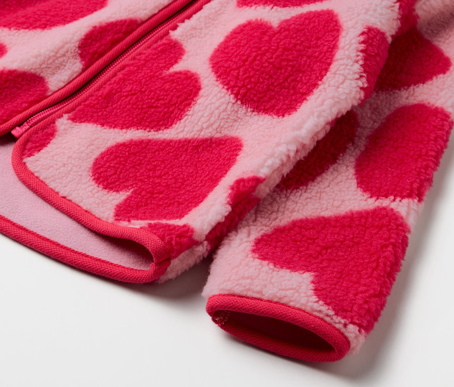 Detailaufnahme einer rosa Fleecejacke mit rotem Herzmuster.
