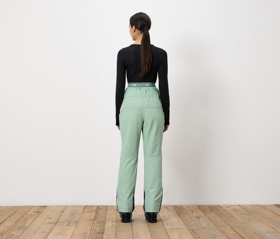 Eine Frau mit dem Rücken zur Kamera trägt ein schwarzes Langarmshirt und hellgrüne Hosen.