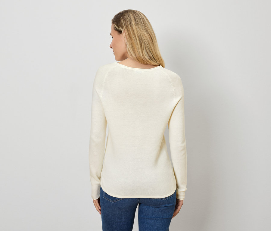 Frau mit blonden Haaren steht mit dem Rücken zur Kamera und trägt einen cremefarbenen Pullover und Jeans.