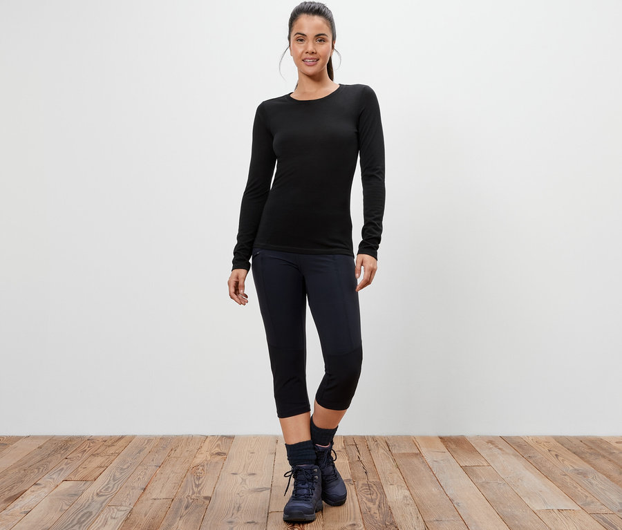 Frau steht und trägt ein schwarzes Langarmshirt mit Merinowolle.
