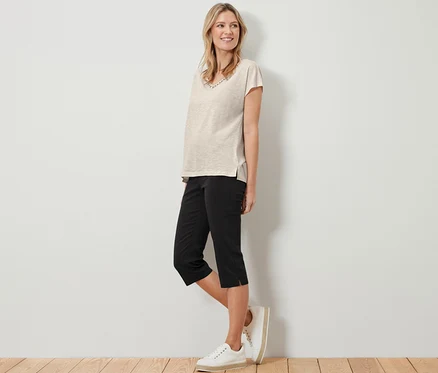 Frau steht und trägt ein beige T-Shirt und eine schwarze 3/4-Stretchhose.