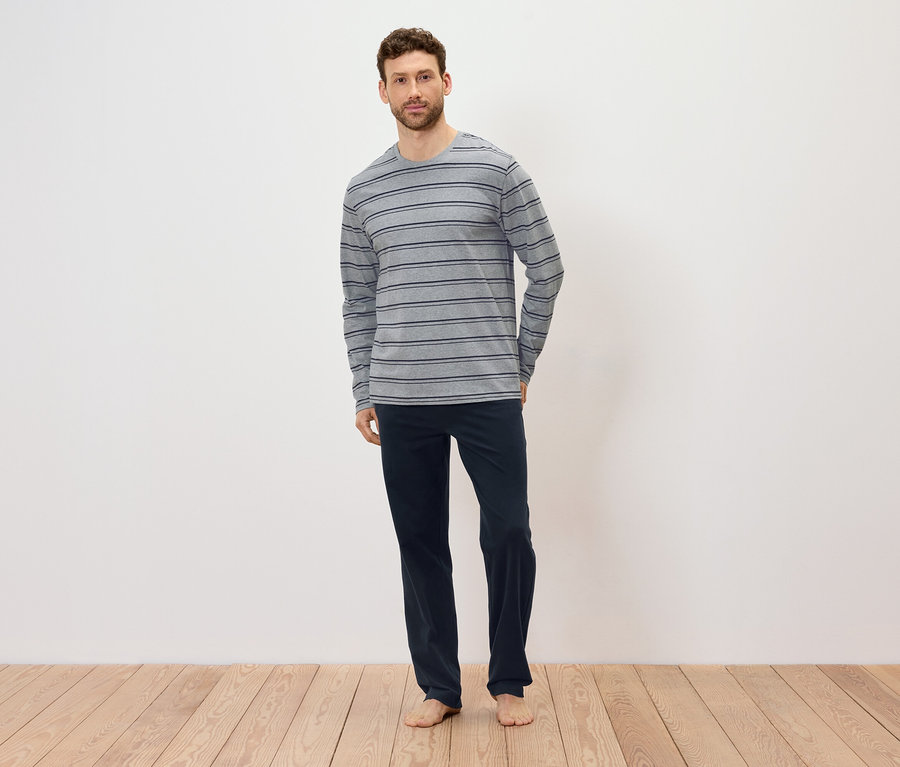 Mann steht barfuß auf Holzboden, trägt ein grau-gestreiftes Langarmshirt und dunkelblaue Hosen.