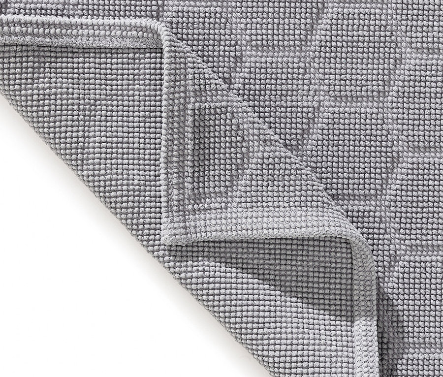 Nahaufnahme einer grauen Badematte mit geometrischem Muster, die teilweise umgeklappt ist.