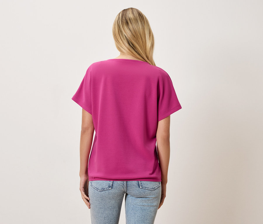 Rückansicht einer Frau mit blonden Haaren, die ein pinkes T-Shirt und hellblaue Jeans trägt.