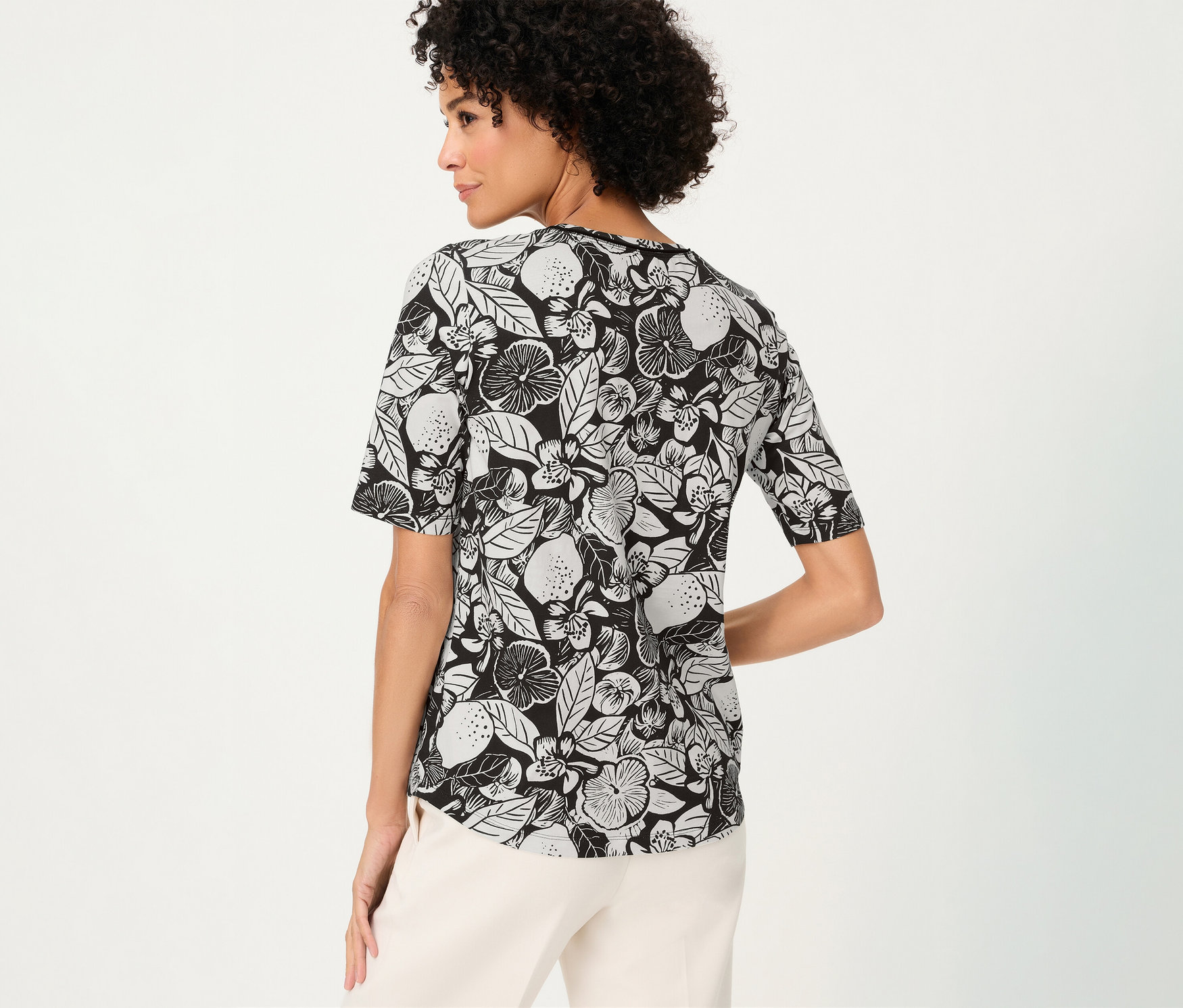 Frau von hinten mit gemustertem Olsen Shirt in Schwarz-Weiß und heller Hose.