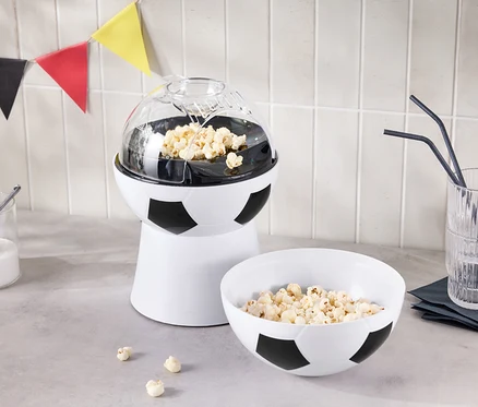 Ein Popcorn-Maker in Fußballoptik steht neben einer Schüssel Popcorn und einem Glas mit Strohhalmen.