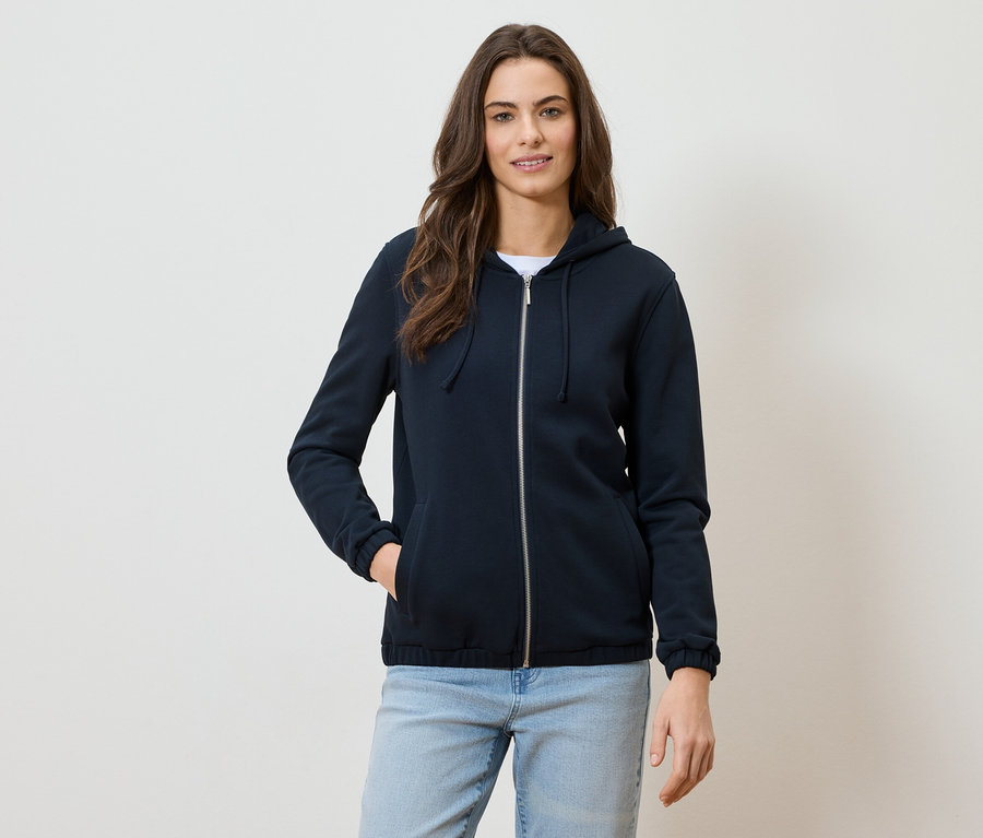Frau mit marineblauer Kapuzenjacke mit Reißverschluss und Jeans.