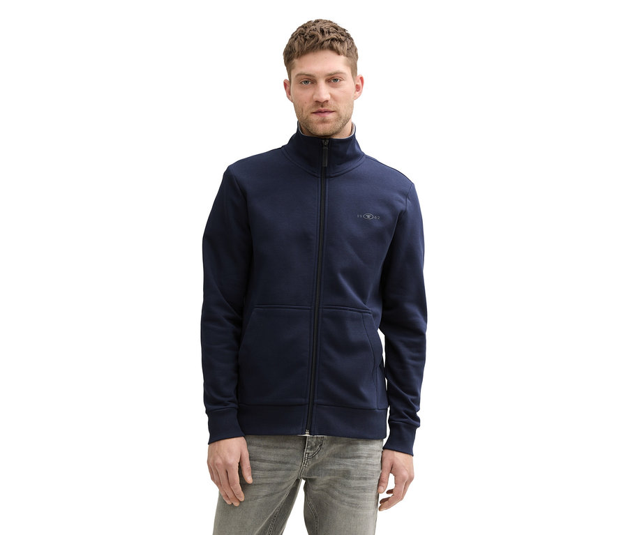 Mann mit Tom Tailor Sweatjacke mit Stehkragen in Sky Captain Blue und grauen Jeans.