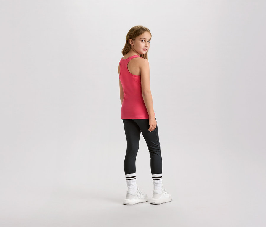 Ein junges Mädchen blickt über ihre Schulter, sie trägt ein rosafarbenes Tanktop, Leggings und weiße Turnschuhe.