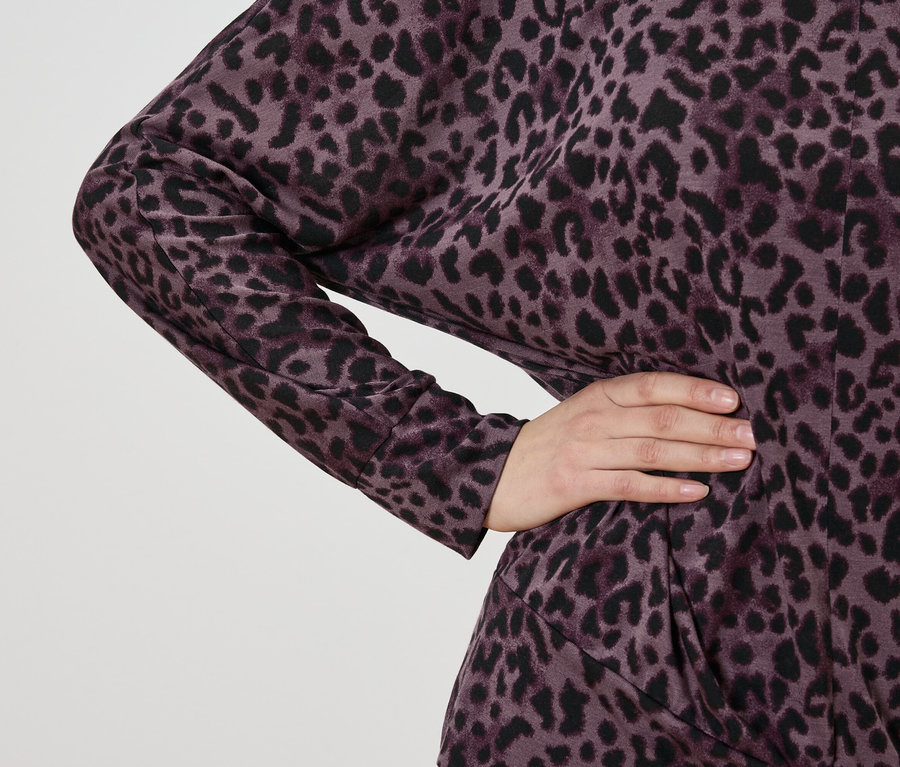Nahaufnahme einer Frau, die ein Kleid mit violettem Leopardenmuster trägt und die Hand in die Hüfte stemmt.