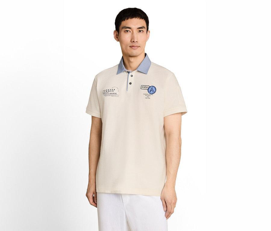 Mann in beigem Poloshirt mit hellblauem Kragen und blauen Aufnähern, dazu weiße Hose.