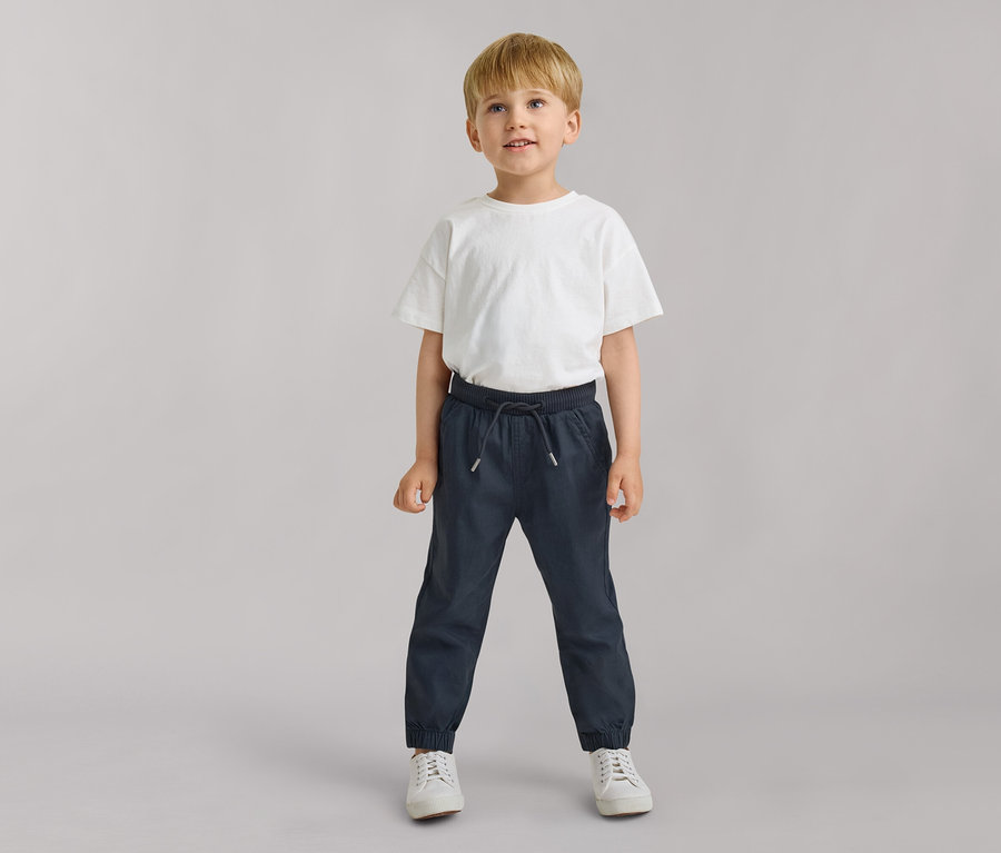 Junger Junge trägt ein weißes T-Shirt und dunkelblaue Kinder-Pull-on-Pants – Fit „Anton“, blickt leicht nach oben.