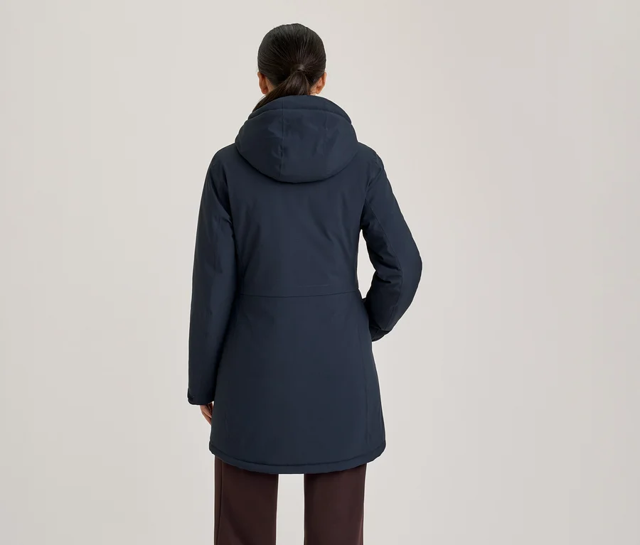 Frau von hinten in einer dunkelblauen Kapuzenjacke und dunklen Hose.