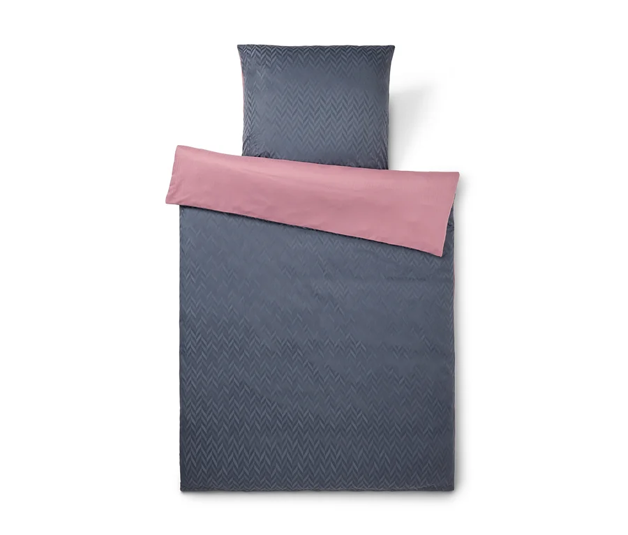 Dunkelgraue Bettwäschegarnitur mit Chevron-Muster und rosa Rückseite. Der Bettbezug ist umgeschlagen, um die rosa Seite zu zeigen.