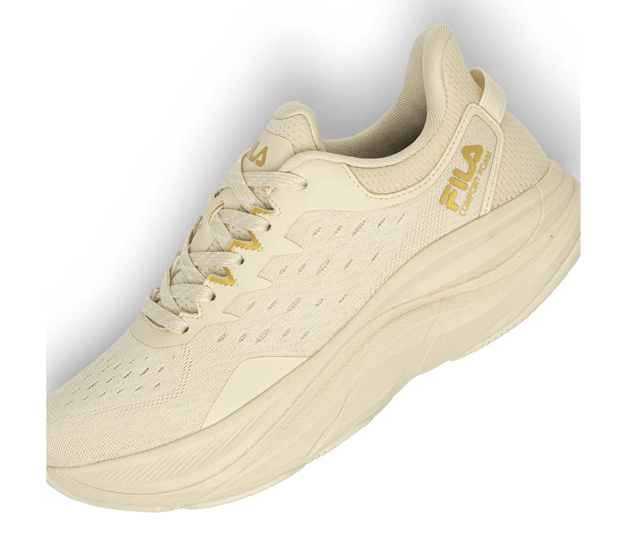 Ein einzelner hellbeiger Sneaker mit Mesh-Obermaterial und dicker, strukturierter Sohle. Ein goldenes Fila-Logo und der Schriftzug „COMFORT FOAM“ sind an der Seite sichtbar. Die Schnürsenkel sind beige mit goldenen Akzenten.