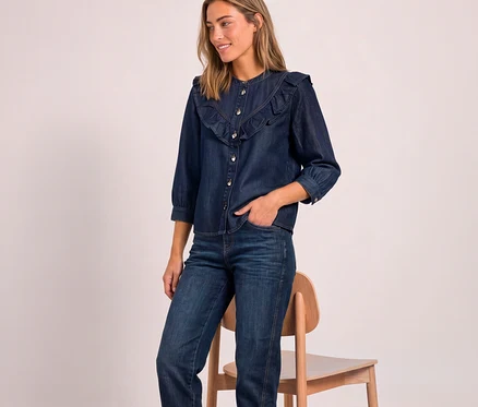Lächelnde Frau trägt eine dunkelblaue Street One Jeansbluse mit Rüschen und Dreiviertelärmeln sowie eine Jeans, eine Hand in der Tasche.