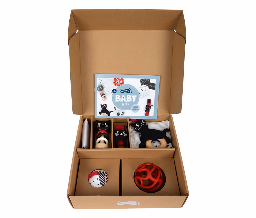 Offene small foot Baby-Box, 0–3 Monate, mit zwei schwarzen Katzenrasseln, einer schwarzen Katzenplüschfigur, einem gemusterten Ball und einer roten Kugelrassel.