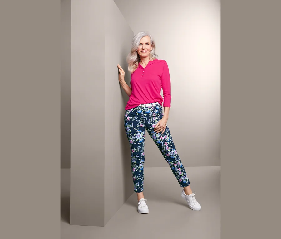 Frau, die sich an eine Wand lehnt, trägt ein pinkfarbenes Oberteil und eine bedruckte Bengalin-Hose.