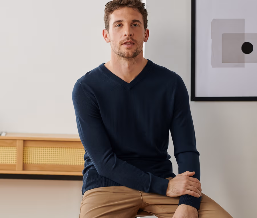 Mann sitzt auf einem Barhocker und trägt einen marineblauen Merinopullover.