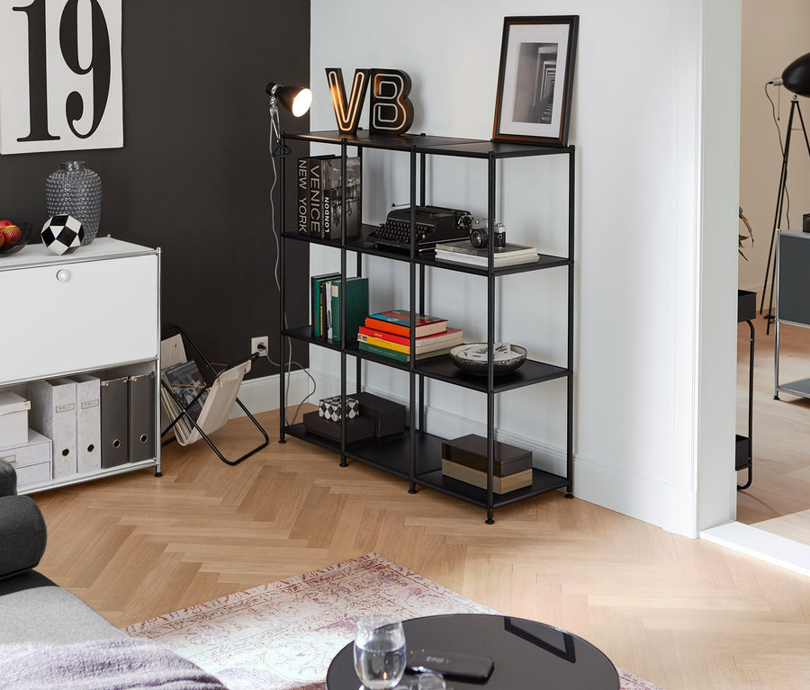 Einrichtungsszene mit Schreibtisch Metall »CN3« mit Klapptür, weiß, einem offenen Regal Metall »CN3«, all black und einem Magazinhalter.