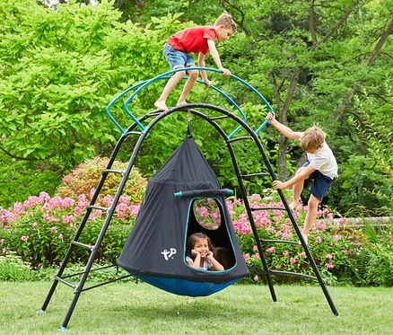 Zwei Jungen klettern auf ein schwarzes und blaues TP Toys Kletterschaukel »UFO«, während ein Mädchen drinnen sitzt.
