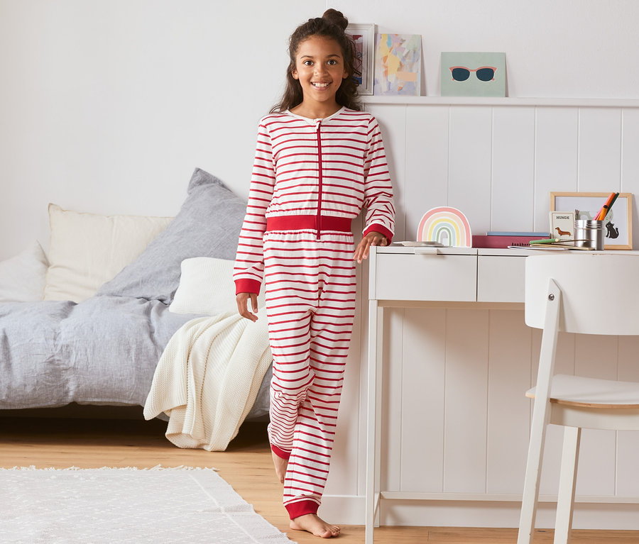 Mädchen steht im Onesie-Pyjama aus Bio-Baumwolle im Schlafzimmer.