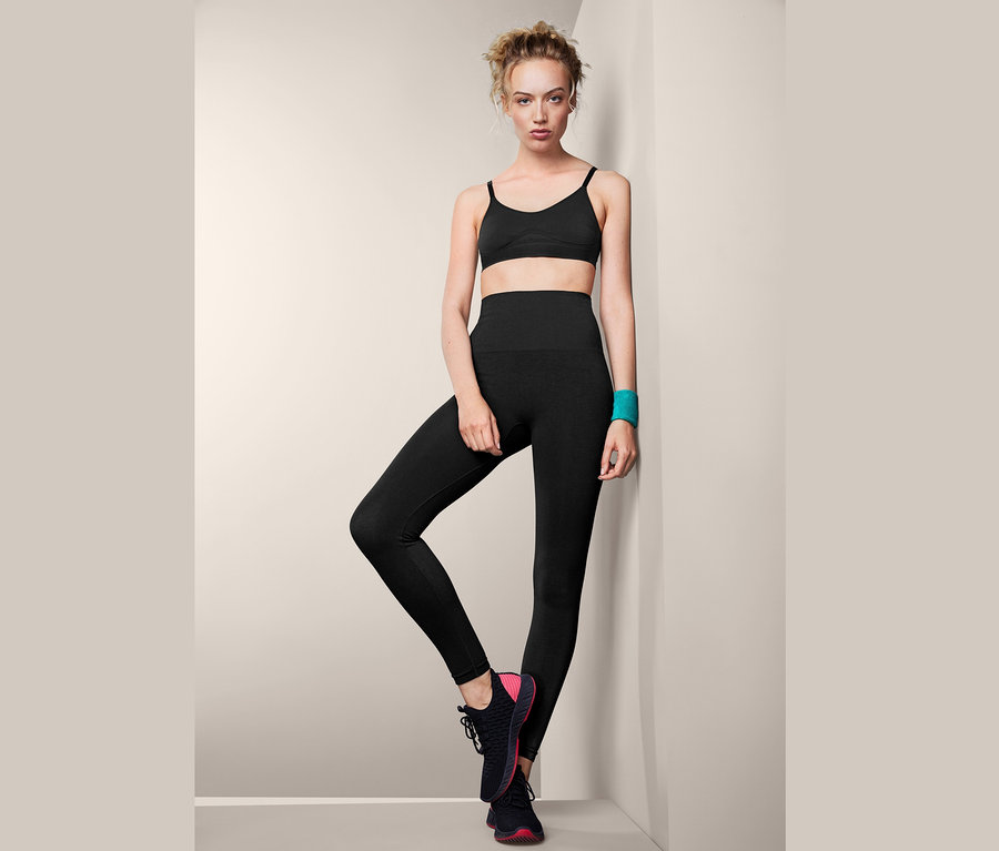 Frau, an eine Wand gelehnt, trägt Seamless-Thermotight, einen Sport-BH und Turnschuhe.