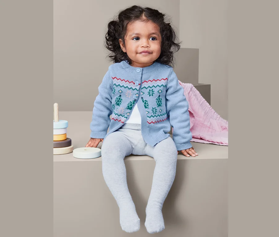 Kleinkind sitzt und trägt eine Strickjacke.