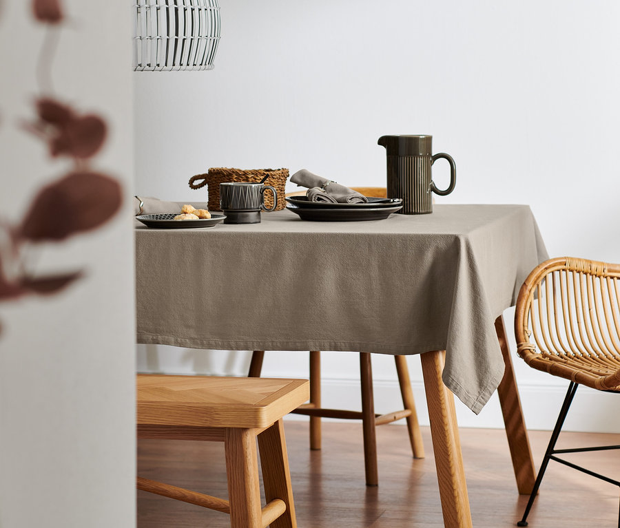 Gedeckter Tisch mit normalgroßer Leinenmischung-Tischdecke in Beige, Tellern, Krug und Weidenkorb.