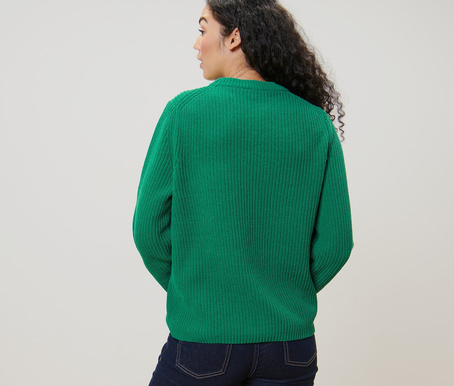 Frau blickt über die Schulter und trägt einen grünen Grobstrickpullover und Jeans.