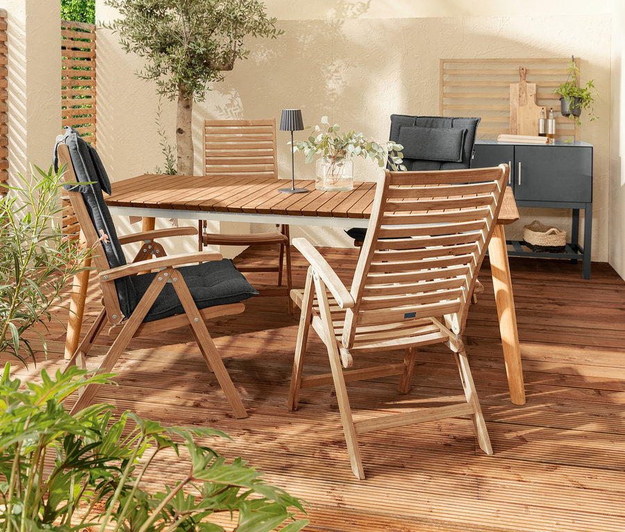 Außenterrasse mit Teak-Ausziehtisch, Stühlen mit anthrazitfarbenen Premium-Hochlehnerauflagen und schwarzer LED-Akku-Tischleuchte. Im Hintergrund Outdoor-Küchenmodul mit Lamellen-Wand.