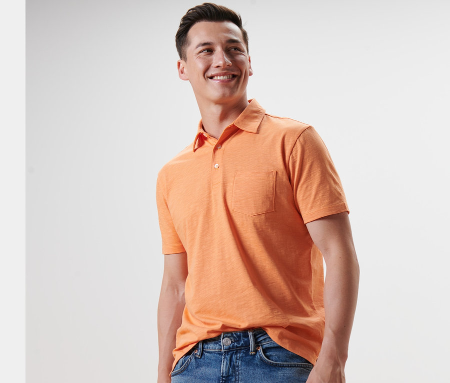 Ein lächelnder Mann trägt ein orangefarbenes Jersey-Poloshirt und Jeans.