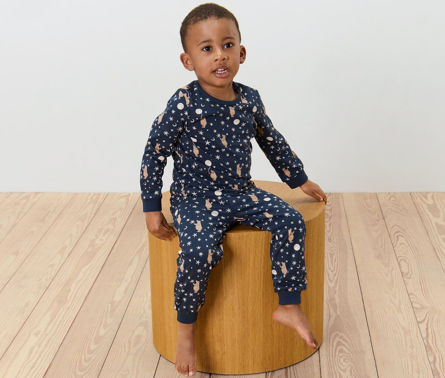 Ein Junge sitzt auf einem Hocker und trägt einen Kinder-Pyjama mit Print.