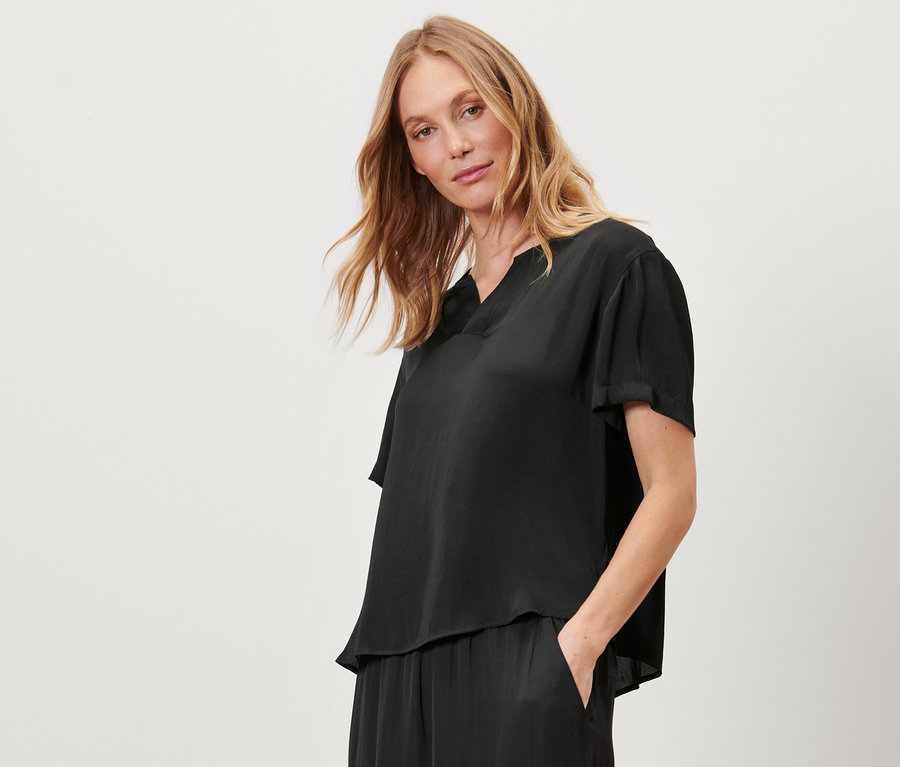 Eine Frau steht mit der Hand in der Tasche einer schwarzen Satin-Tunikabluse.