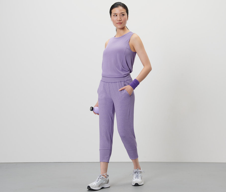 Eine Frau steht und hält eine lila Wasserflasche. Sie trägt ein lila Oberteil und eine 3/4-Sporthose, lila.