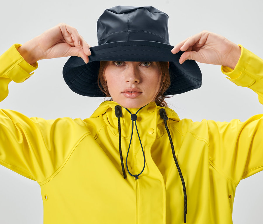 Frau richtet einen Unisex-Regenhut und trägt eine gelbe Jacke.