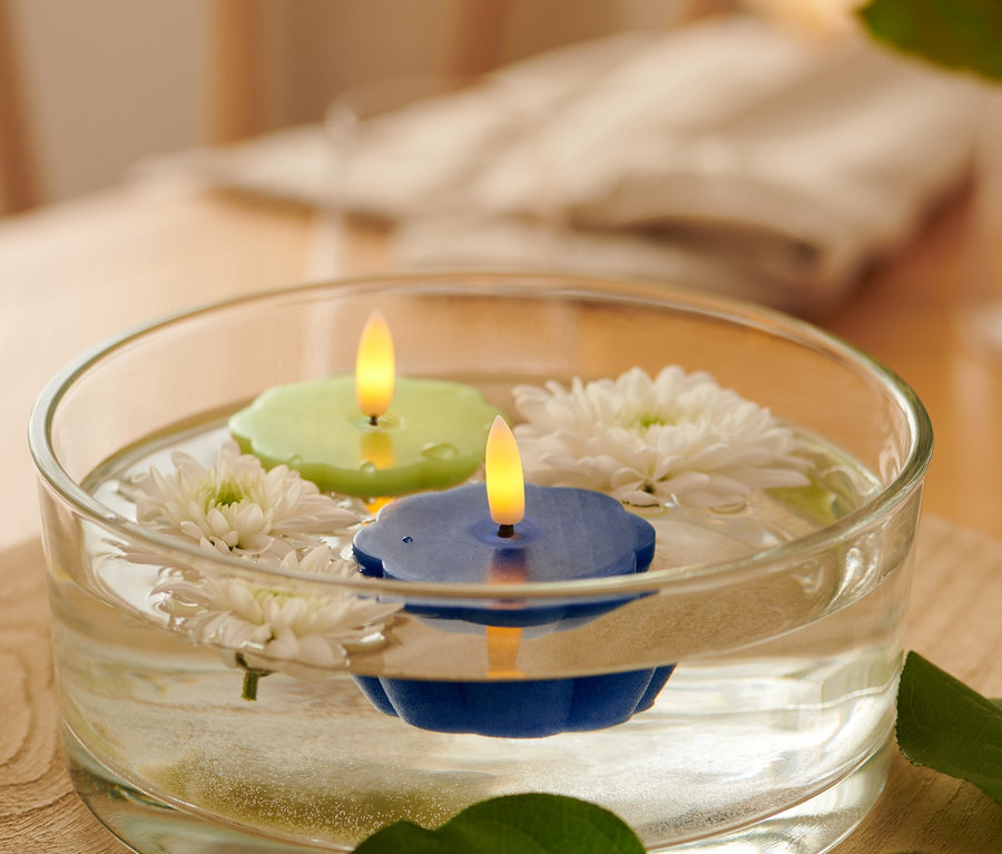 In einer Glasschale schwimmen zwei LED-Echtwachs-Teelichter, ein grünes und ein blaues, und weiße Blumen.