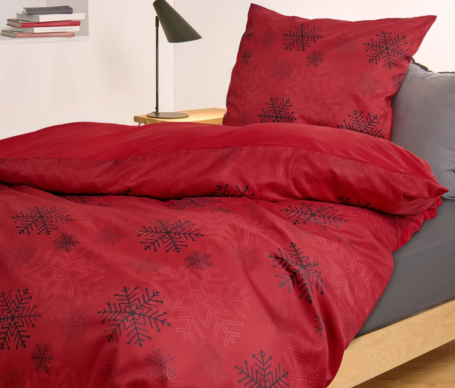 Rote Microfaser-Flanell-Bettwäsche mit Schneeflockenmuster liegt auf einem Bett.