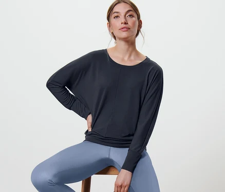 Frau sitzt auf einem Hocker und trägt ein marineblaues Sport-und-Yogashirt.
