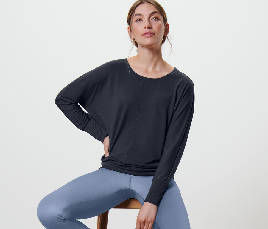 Frau sitzt auf einem Hocker und trägt ein marineblaues Sport-und-Yogashirt.