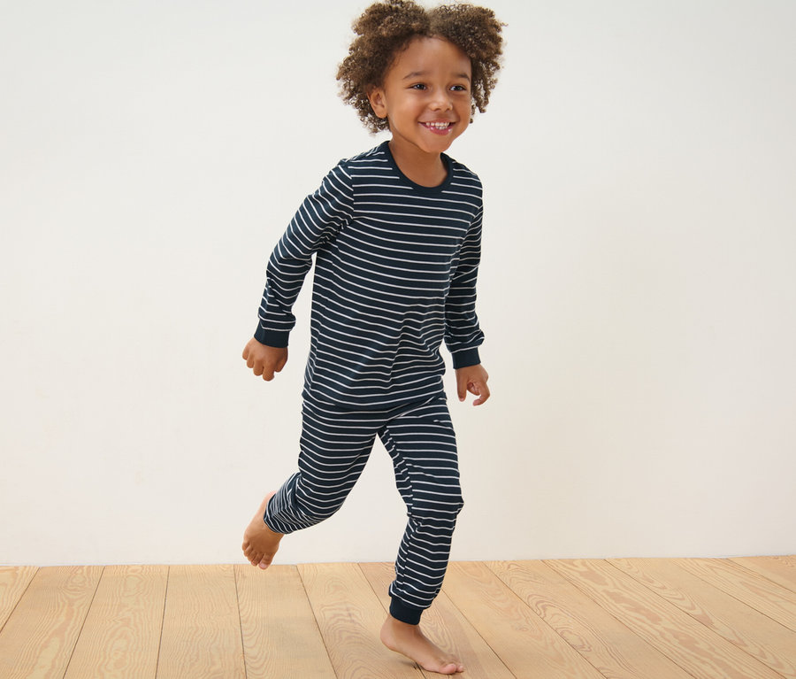 Ein Junge in einem blau gestreiften Pyjama rennt auf einem Holzboden. 2 Kinder-Pyjamas, blau.