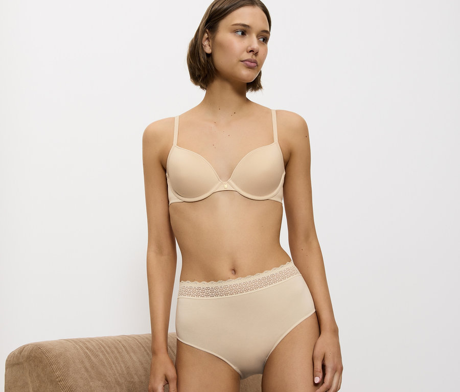 Frau kniet auf einem braunen Sofa in einem beigen BH und Slip.