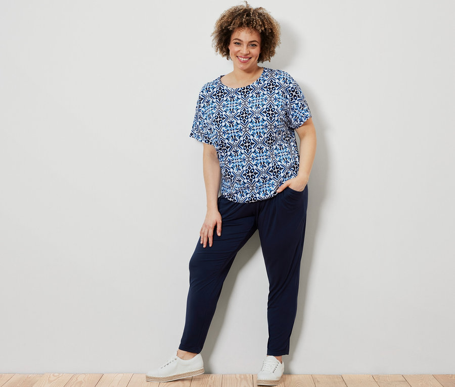 Frau posiert in blauem, bedrucktem Blusenshirt und dunkelblauer Jerseyhose.